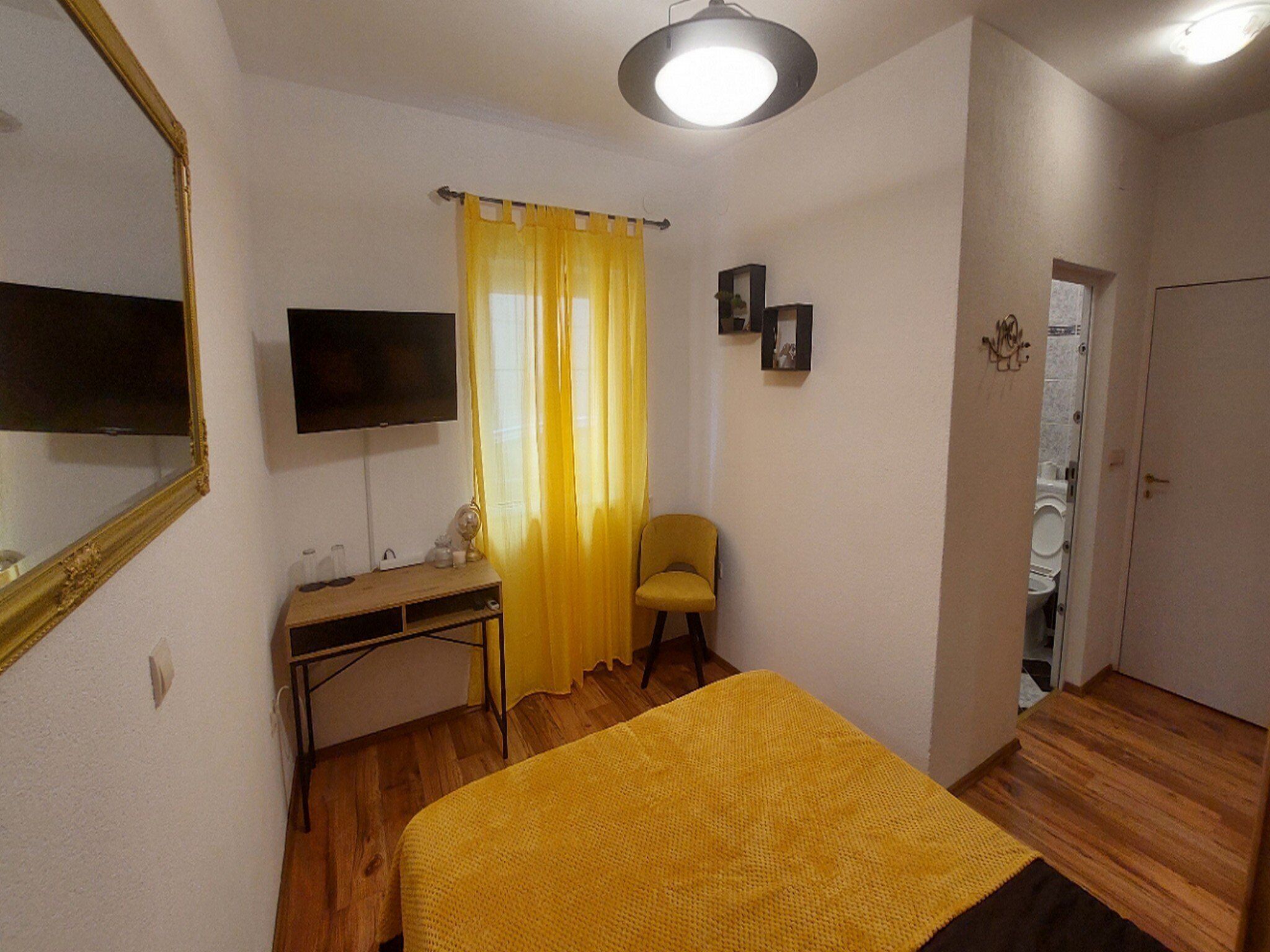 Un dormitorio con cama, escritorio, silla, televisor y puerta que da a un baño.