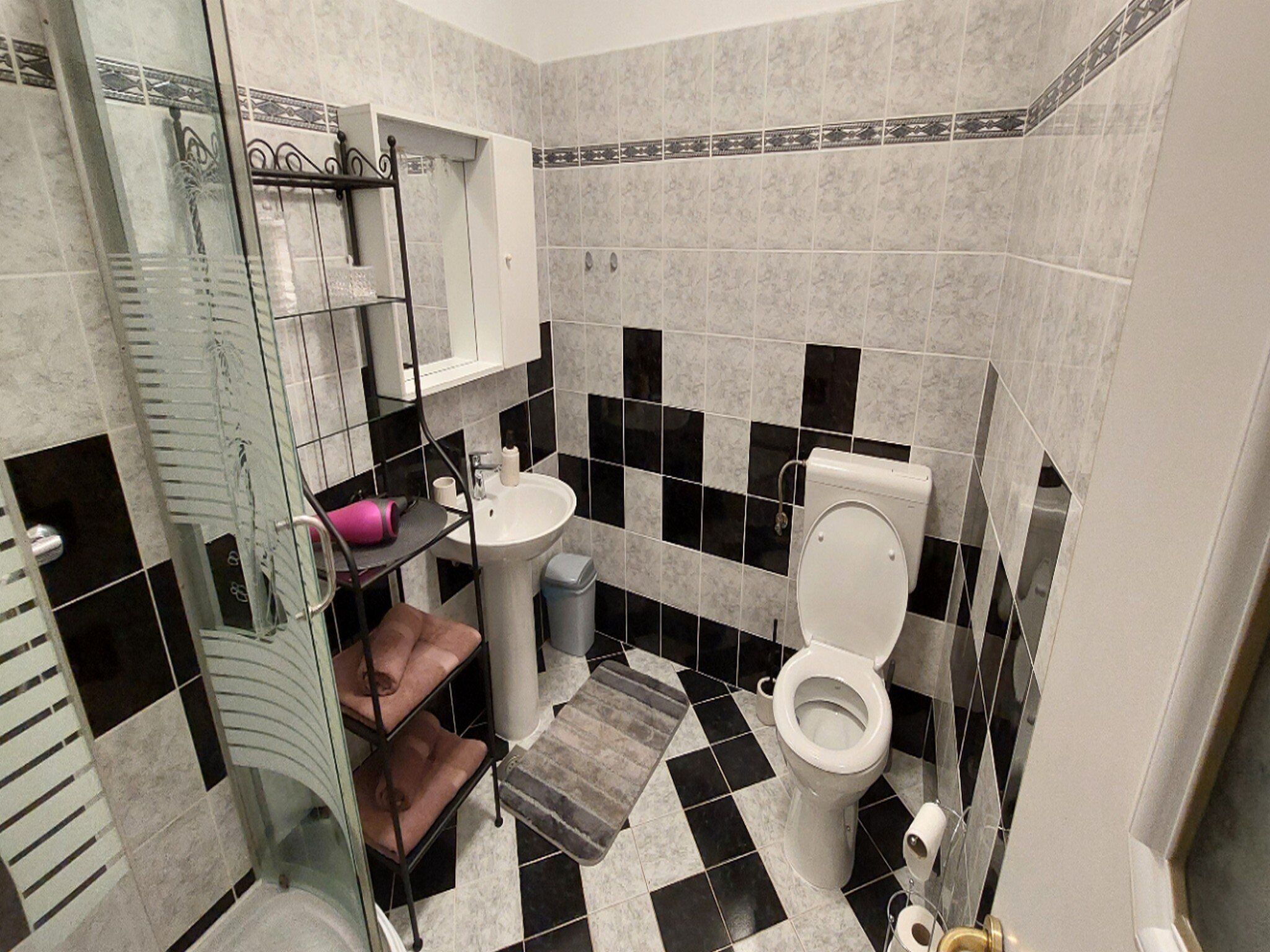 A bathroom with a black and white checkered floor, a white sink, a toilet, and a glass shower enclosure.