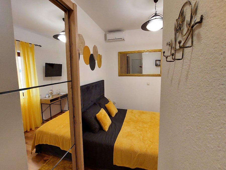 A bedroom with a bed, a desk, a chair, a television, and a mirror.