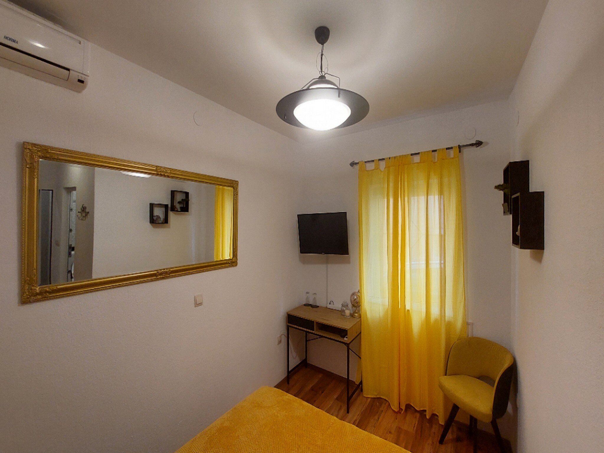 A room with a bed, a desk, a chair, a television, and a mirror.
