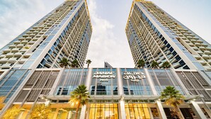 Un edificio de gran altura con un diseño arquitectónico moderno, que cuenta con dos torres destacadas con balcones y una entrada central con señalización.