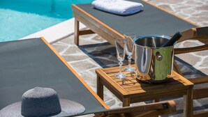 Ein Liegebereich am Pool mit einem Holztisch, einem Metallkübel, zwei Gläsern und einem gefalteten Handtuch.