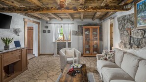 Ein rustikales Wohnzimmer mit Steinböden, Holzbalkendecke, einer Couch, einem Couchtisch und einer Vitrine mit Glastüren.