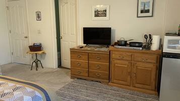 A compact kitchen with a microwave, stove, and wooden cabinets. A television is mounted above the stove, and a small table with a basket is visible near the door.
