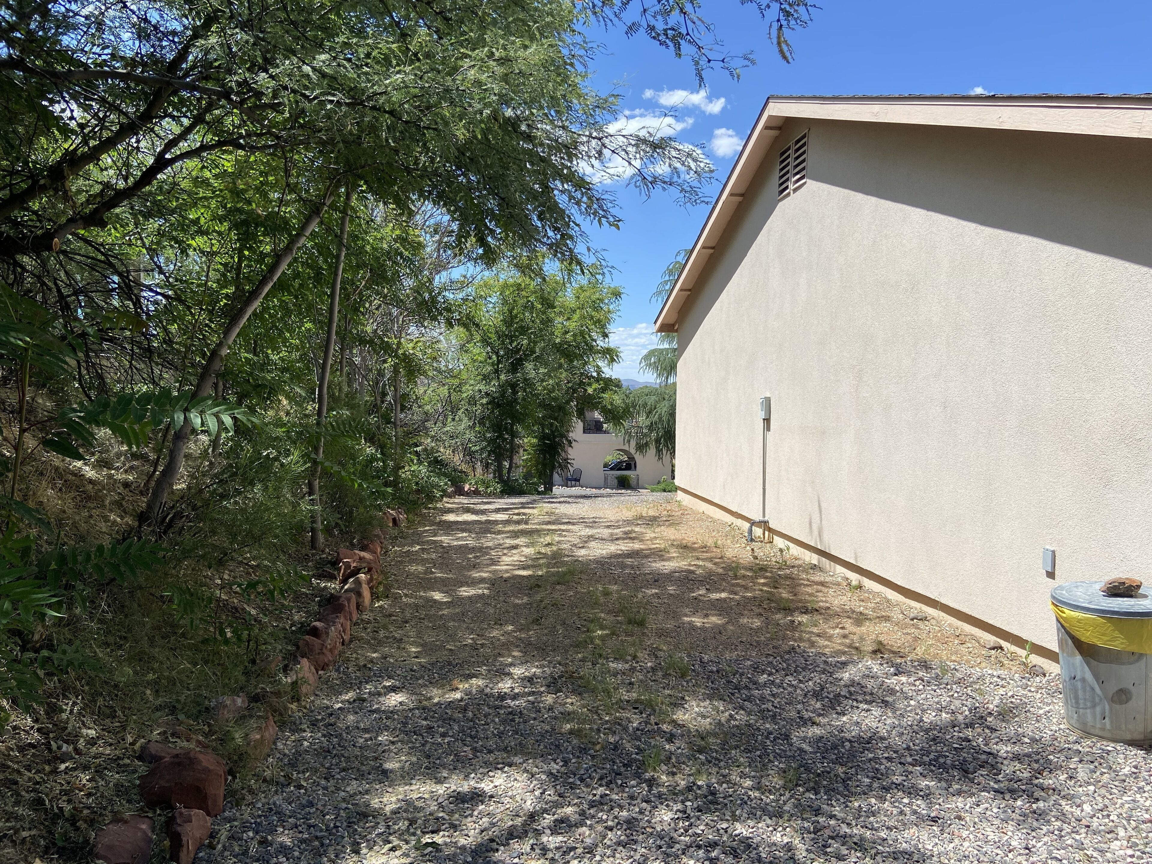 A gravel path leading to a building with a beige exterior and a small trash bin on the right.