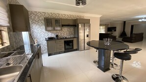 A modern kitchen with a central island, stainless steel appliances, and a dining area with bar stools. - Iter Away Highland Lodge (Nyanga)