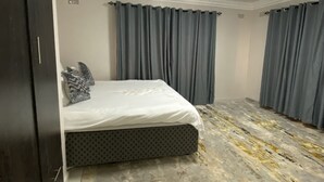 A bedroom with a bed, curtains, a ceiling light, and a patterned carpet. - Iter Away Highland Lodge (Nyanga)