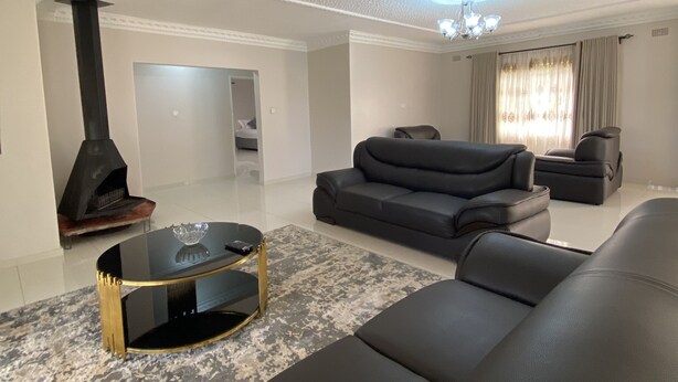 A modern living room with a black leather sofa, a glass coffee table, and a fireplace. - Iter Away Highland Lodge (Nyanga)