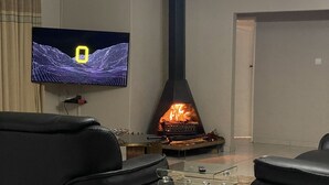 A living room with a fireplace, a television, and two black sofas. - Iter Away Highland Lodge (Nyanga)