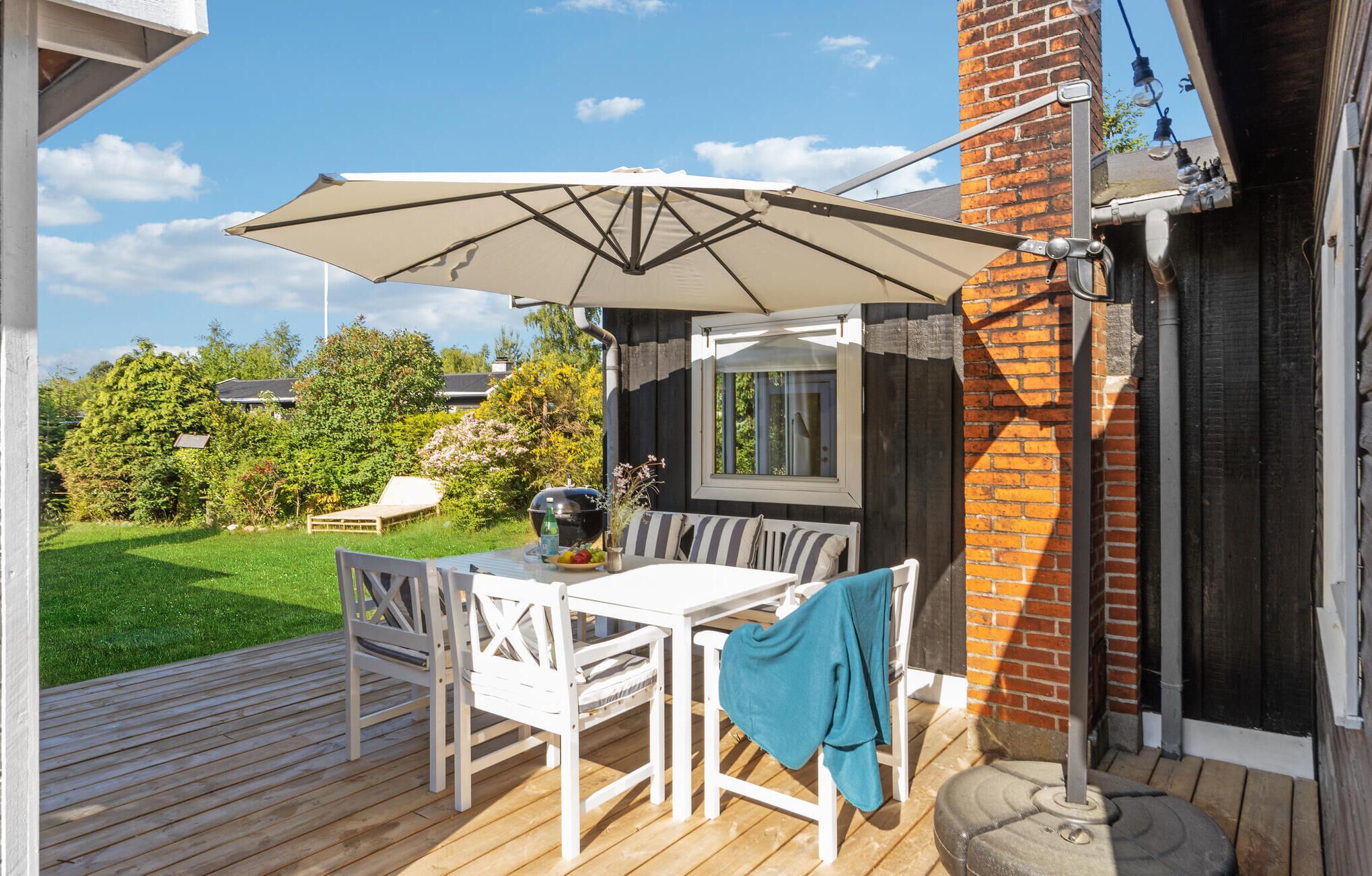 Une terrasse avec une table et des chaises, un barbecue et un grand parasol.