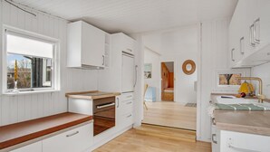 Moderni keittiö, jossa on valkoiset kaapit, puinen työtaso ja näkymä viereiseen ruokailutilaan.