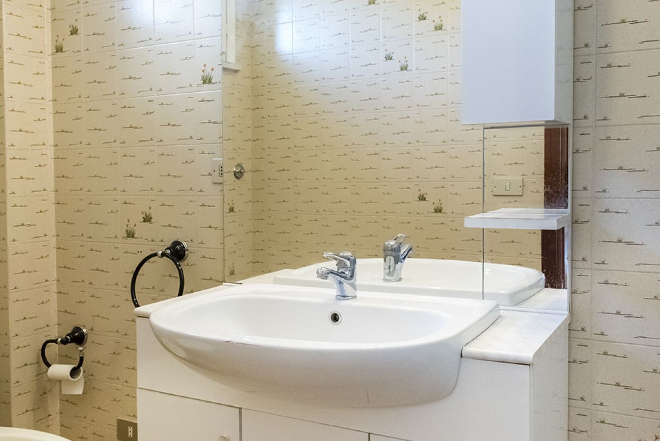 Une salle de bain avec un lavabo blanc, deux robinets, un porte-serviettes et un support à papier toilette.