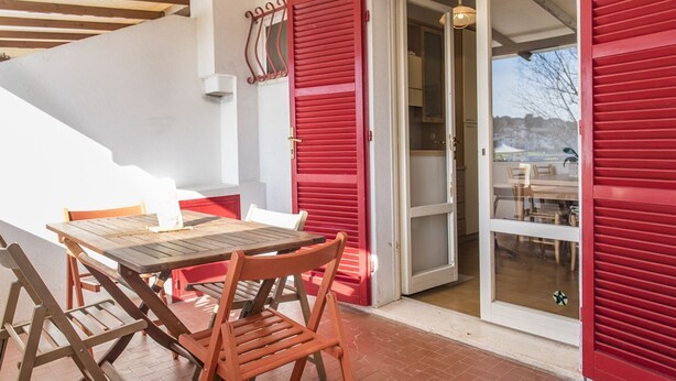 Una mesa de madera con sillas, una puerta roja y una puerta de cristal que da a un área exterior.