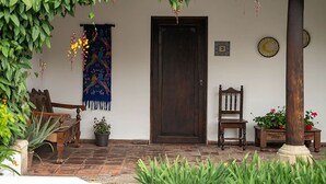 A covered porch with a wooden bench, a chair, and potted plants. - Casita Tumbergia (Antigua Guatemala)