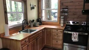 A kitchen with wooden cabinets, a stainless steel sink, a stove, and two windows offering views of the outdoors.