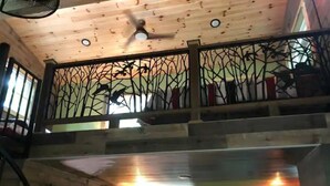 A multi-level room with a wooden ceiling, a balcony with decorative metal railings, and a ceiling fan.