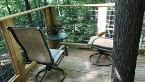 A wooden deck with two chairs and a small table, surrounded by a metal railing and trees.