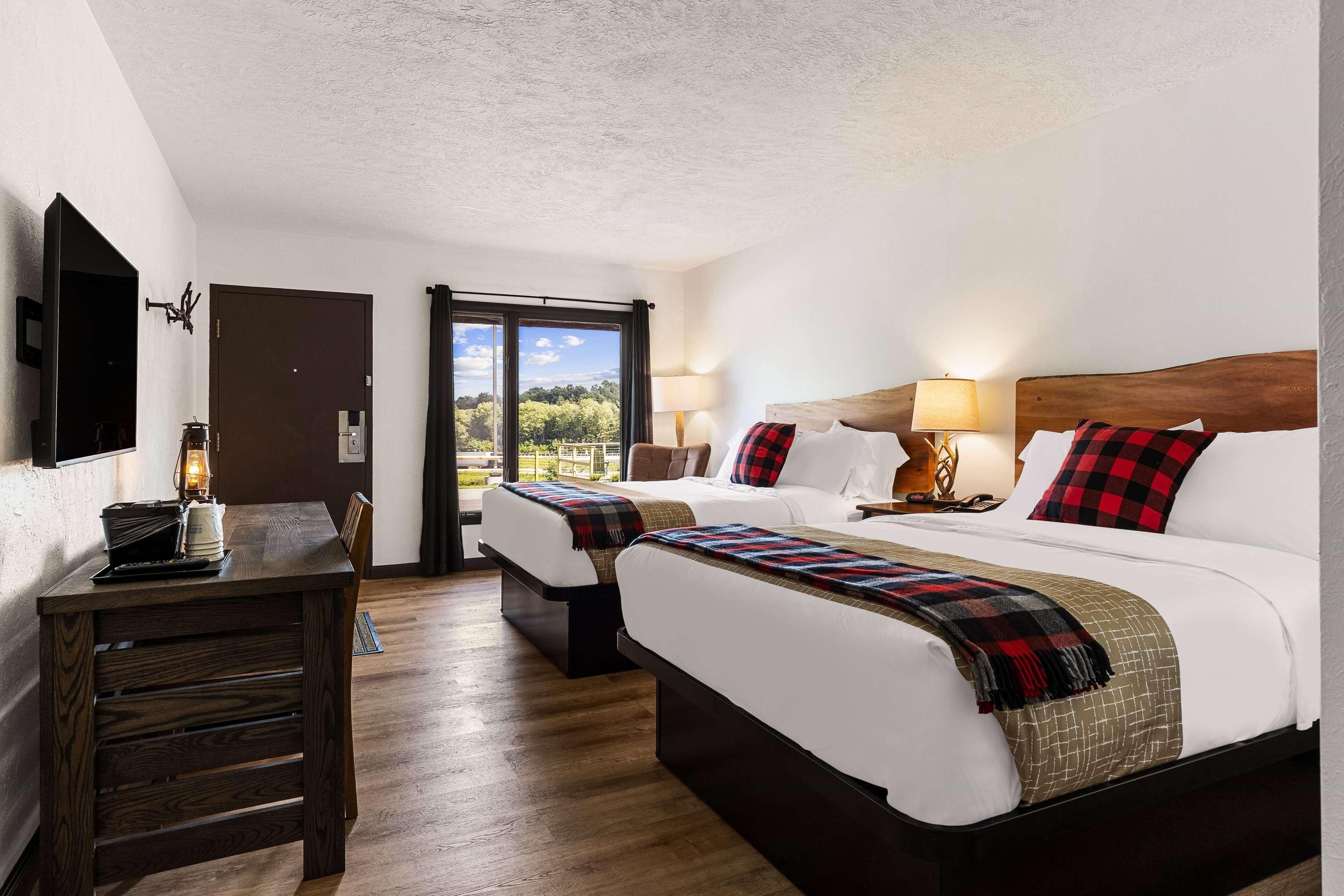 Habitación de hotel con dos camas, un escritorio de madera y vistas a zonas verdes.