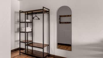 Una habitación de esquina con piso de madera, una estantería metálica con toallas y un espejo con marco de madera.