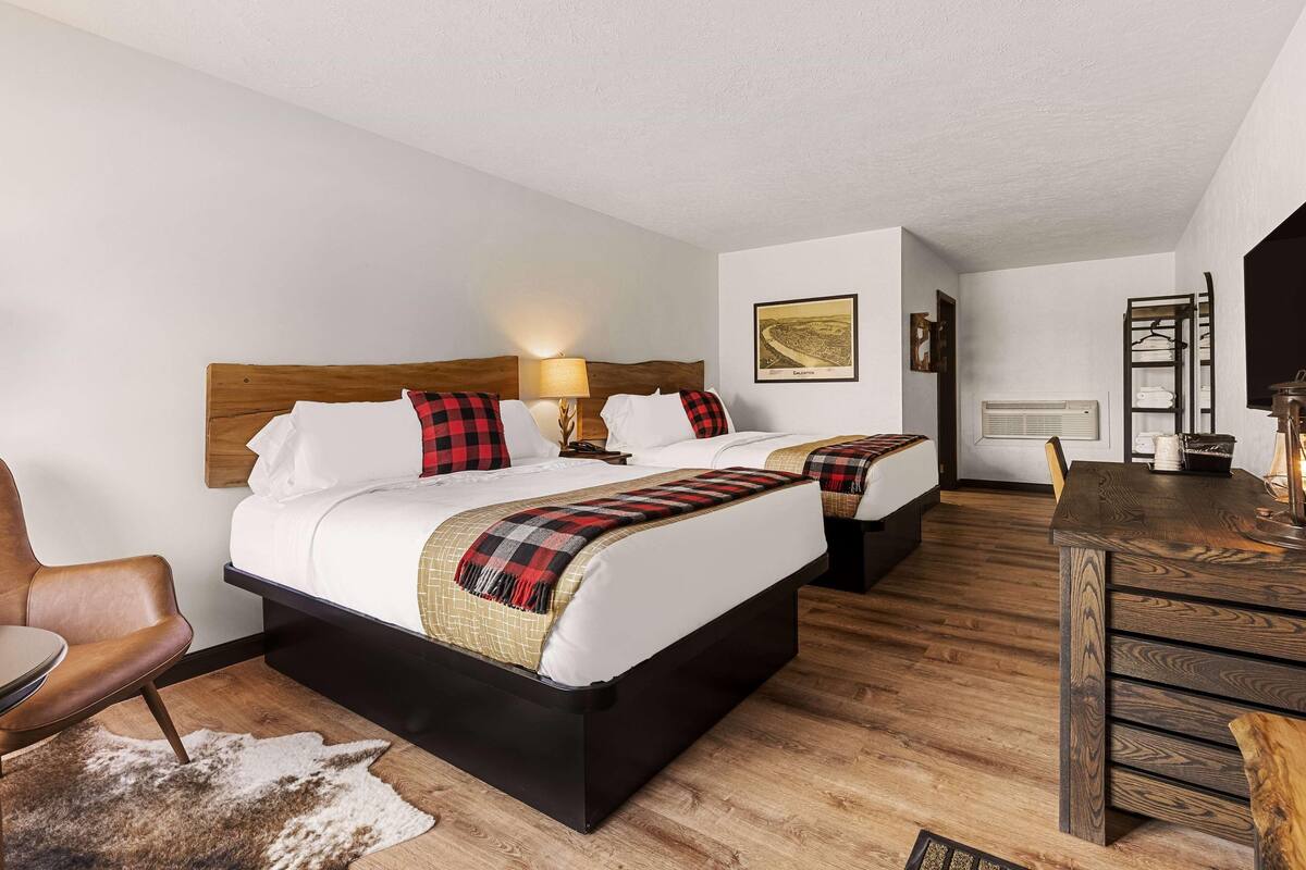 Une chambre d’hôtel avec deux lits, un bureau en bois, une chaise et un tapis en peau de vache.