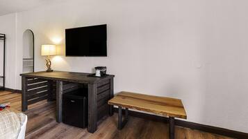 A room with a wooden desk, a bench, a TV mounted on the wall, and a lamp.