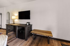 Une pièce avec un bureau en bois, un banc, un téléviseur fixé au mur et une lampe.