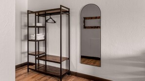 A corner room with a wooden floor, a metal shelving unit with towels, and a mirror with a wooden frame. - Travelodge By Wyndham Emlenton (Emlenton)