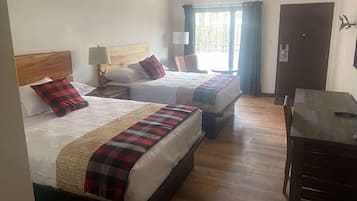 Habitación de hotel con dos camas, suelo de madera, un escritorio y una ventana con cortinas.