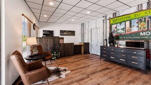 Un espace d’accueil comprenant un comptoir de réception en bois, une console noire et un guichet d’accueil. Au-dessus du guichet, on peut lire une pancarte sur laquelle est inscrit : « Bienvenue au motel Emelina. »