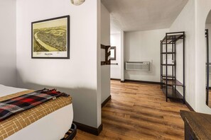 Une chambre d’hôtel avec un lit, une carte encadrée accrochée au mur, un plancher en bois et une étagère en métal.