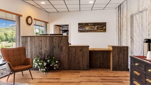 A reception area with a wooden reception desk, a clock, and a painting on the wall. - Travelodge By Wyndham Emlenton (Emlenton)