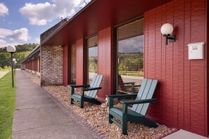 Un bâtiment aux murs extérieurs rouges, doté de grandes fenêtres et d’un espace extérieur aménagé avec des fauteuils Adirondack.