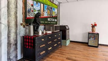 Una habitación con piso de madera, un aparador negro con cajones, una cafetera, un refrigerador y una pared con el letrero 'Welcome to the Motor Inn'.