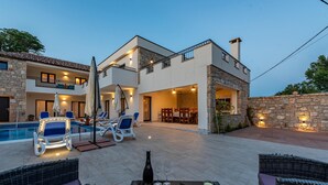 Ein modernes, zweistöckiges Haus mit Swimmingpool, Sitzgelegenheiten im Freien und einer gut beleuchteten Terrasse.