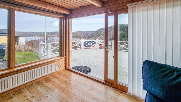 A wooden-paneled room with large windows, a view of a deck and outdoor structures, and a door leading outside. - Cozy home in Uddevalla (Uddevalla)