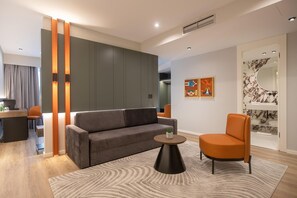 A modern living room with a grey sofa, an orange armchair, a round coffee table, and a patterned rug. - Elisa Hotel Tirana Affiliated By Melia (Tirana)