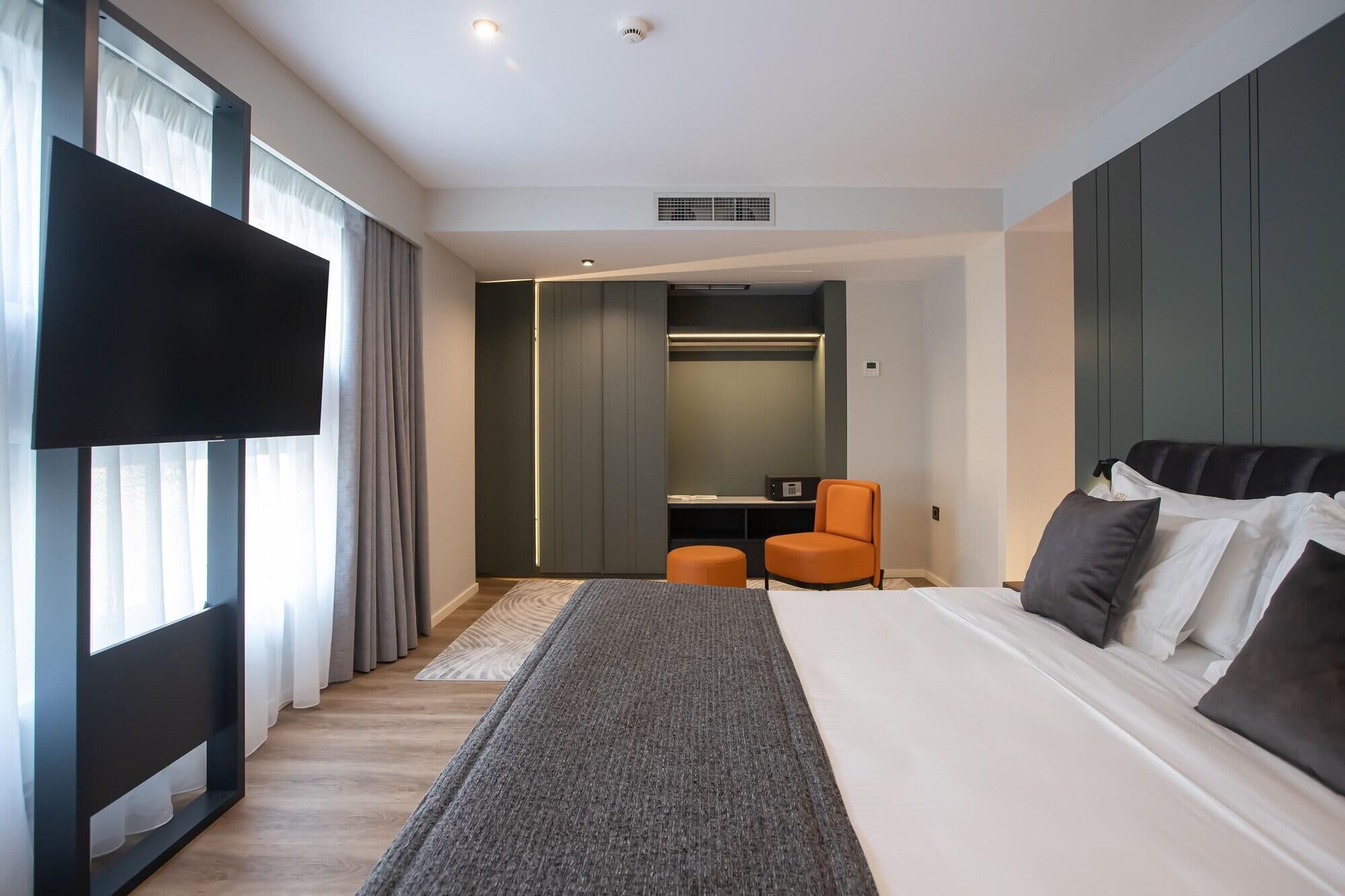 A modern hotel room with a large bed, a flat-screen TV, a seating area, and a walk-in closet.