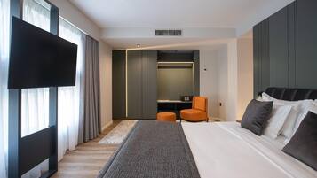 A modern hotel room with a large bed, a flat-screen TV, a seating area, and a walk-in closet.