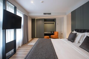 A modern hotel room with a large bed, a flat-screen TV, a seating area, and a walk-in closet. - Elisa Hotel Tirana Affiliated By Melia (Tirana)