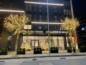 A hotel with a modern facade, illuminated signage, and decorative trees. - Elisa Hotel Tirana Affiliated By Melia (Tirana)