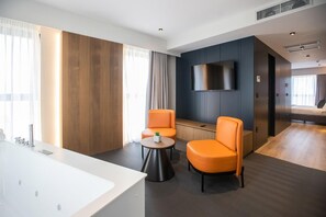 A modern hotel room with a large flat-screen TV mounted on the wall, a white bathtub, and two orange chairs around a small round table. - Elisa Hotel Tirana Affiliated By Melia (Tirana)