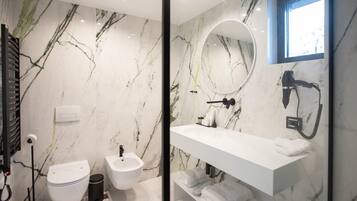 A modern bathroom with a marble backsplash, a white sink, a bidet, and a handheld showerhead.