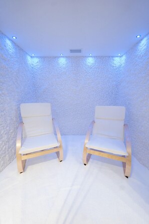 Two white cushioned chairs with wooden frames in a room with textured walls and recessed ceiling lighting. - Elisa Hotel Tirana Affiliated By Melia (Tirana)