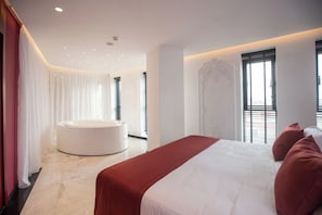 A modern hotel room with a large bed, a circular jacuzzi, and a view of the city through the windows. - Elisa Hotel Tirana Affiliated By Melia (Tirana)