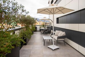 A modern outdoor balcony with a seating area, including a sofa, chairs, and a table. - Elisa Hotel Tirana Affiliated By Melia (Tirana)