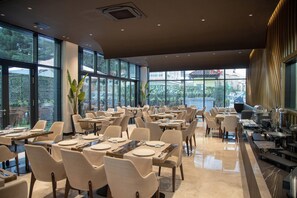 A spacious restaurant with multiple tables and chairs, large windows, and a view of the outside. - Elisa Hotel Tirana Affiliated By Melia (Tirana)
