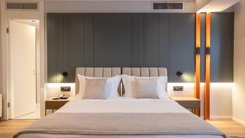 A modern hotel room with a large bed, two bedside tables, a nightstand, and a wall-mounted heater.