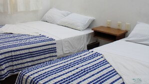Quarto de hotel com duas camas, cada uma com colcha listrada, uma mesinha de cabeceira com abajur e um quadro na parede.
