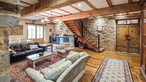 Ein geräumiger Wohnbereich mit Steinwand, Holzbalken, einer Treppe und einer Küche im Hintergrund.