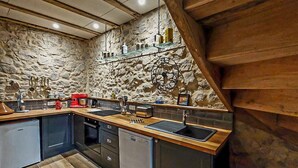 Eine Küche mit Steinwänden, Holzbalken, einem roten Standmixer und einem schwarzen Spülbecken.